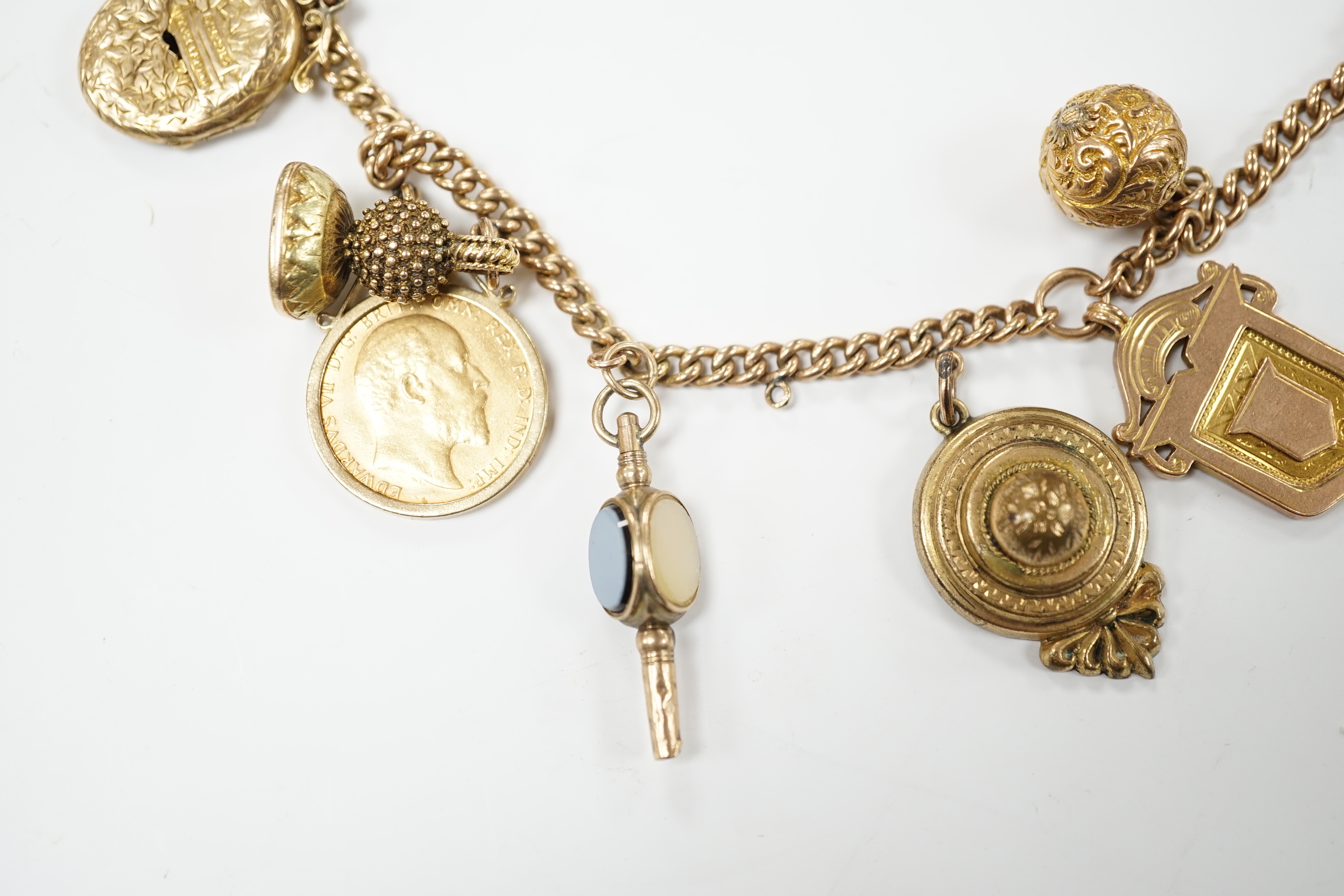 A 9ct gold curblink chain hung with fifteen assorted charms including a 1906 sovereign and an 1865 20 francs coin, gross 80.8 grams